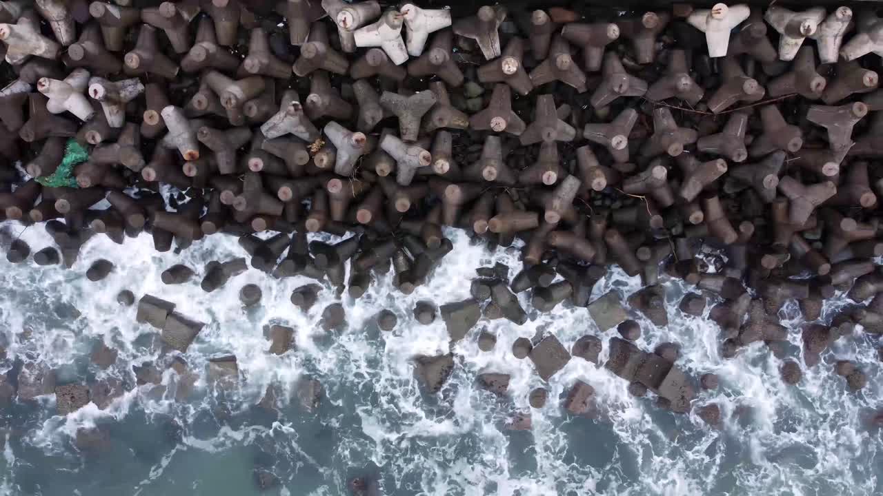 Vista aerea di un'onda marina che si infrange su un blocco di cemento tetraedrico o frangiflutti sulla spiaggia di Glagah, Indonesia.