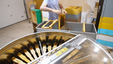 apiculturist takes the frames from a wooden box and places them into metal box. device for honey extraction at foreground.