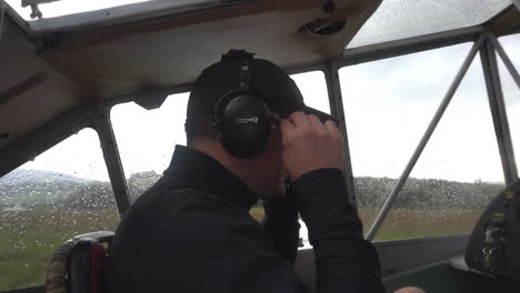 profile close up fhd shot of a male pilot sitting in an open cockpit, adjusting his headphones set and preparing to take off in a light-sport airplane