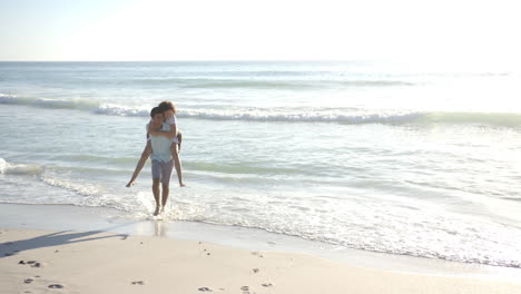 biracial couple enjoys a beach walk, the woman piggybacking on the man with copy space