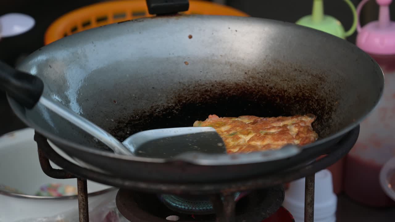 A ladle on top the omelet, a hand uses it to move omelet out and also turns off the fire, Street Food, Thailand
