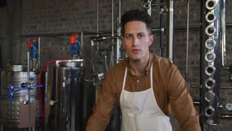 Portrait-of-serious-caucasian-man-working-at-gin-distillery,-using-equipment-and-looking-to-camera