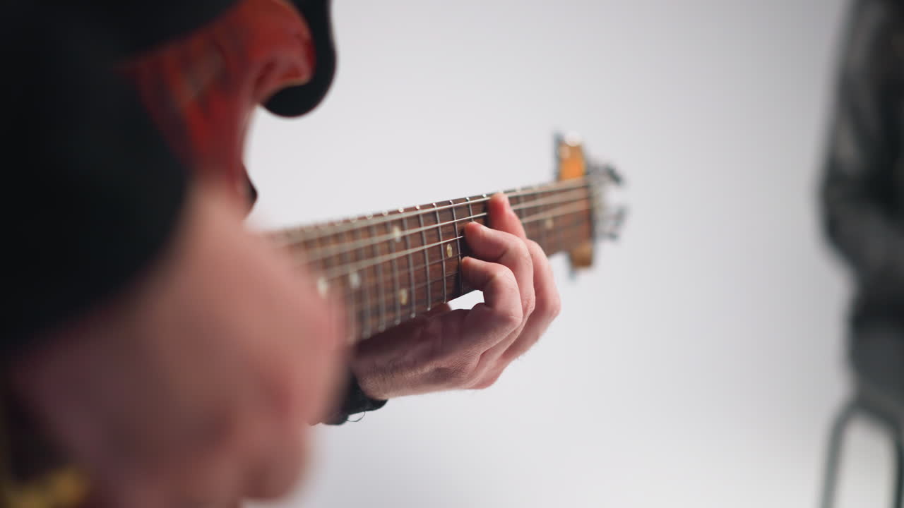 vista cercana de la mano del guitarrista tocando una guitarra roja, detalle enfocado contra un fondo blanco suavemente borroso