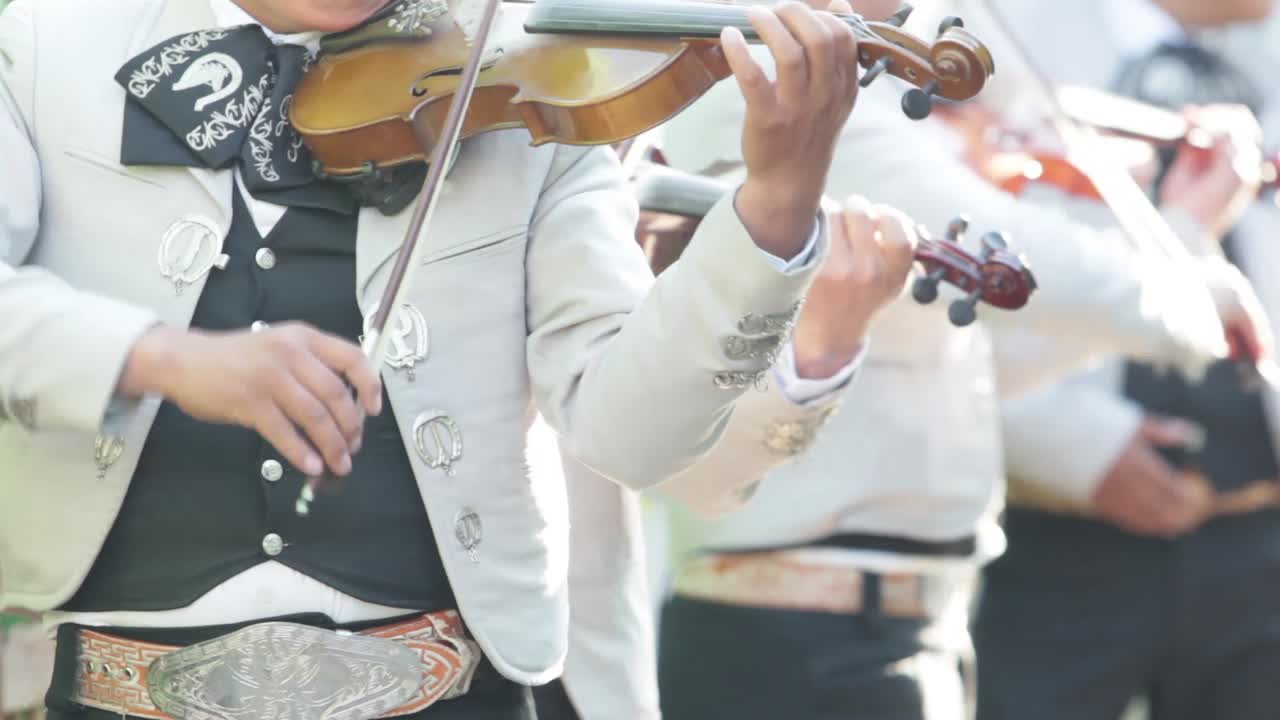three mexican mariachis with white mariachi costume playing the violin at a mexican party