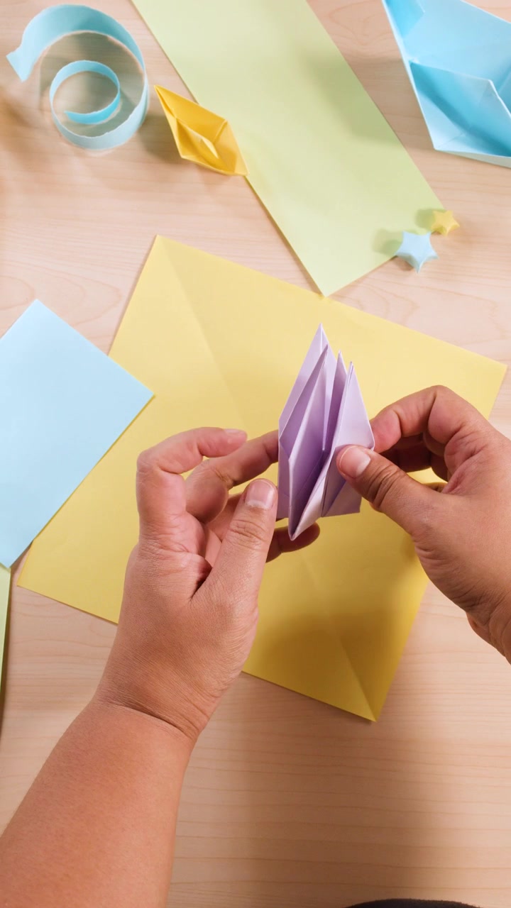 Vista dall'alto di mani che piegano con cura carta viola per formare un uccello origami su una scrivania.