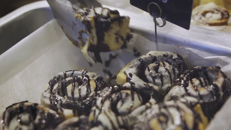 Close Up Of Cinnamon Rolls Frosted With Cream Cheese Icing And Chocolate Syrup Drizzled On Top