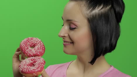 woman holding two pink donuts with sprinkles