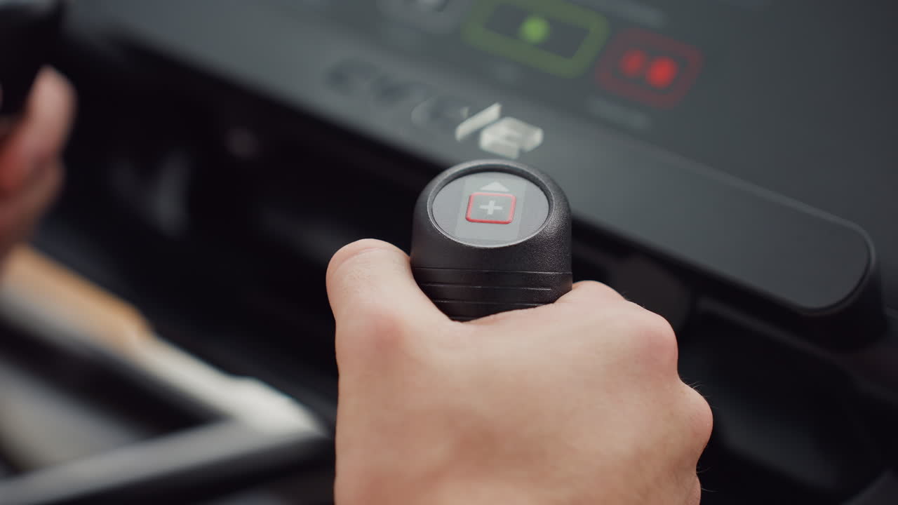 Pressing control knob on elliptical trainer console to adjust workout intensity with firm grip focused wristband visible in sleek modern gym environment under bright natural light