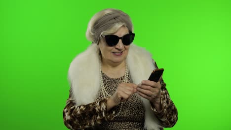 Caucasian-grandmother-woman-using-smartphone,-pointing-at-camera-with-hand