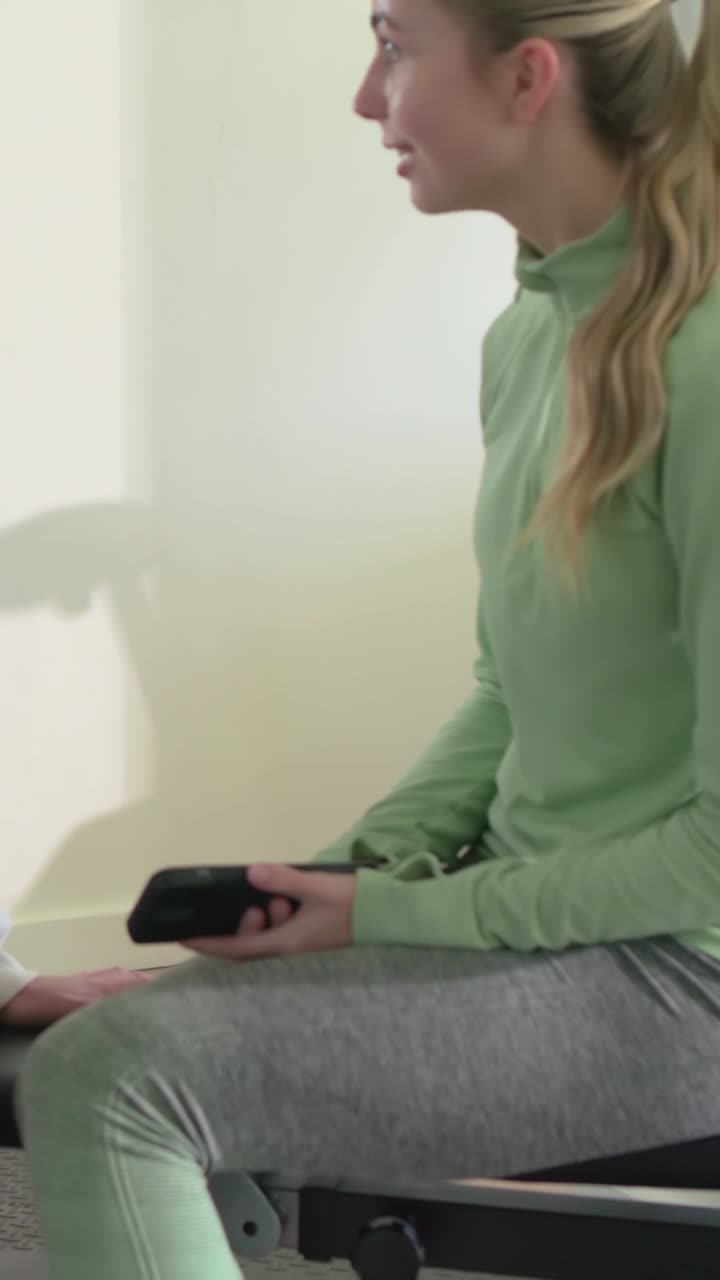 Vertikal video: Kvinde i cremefarvet hættetrøje vender sig og reagerer, da ven kommer ind og viser telefon på bænken.