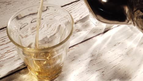 Slow-motion-extreme-closeup-of-tea-pouring-into-a-glass-cup-on-a-distressed-wood-table