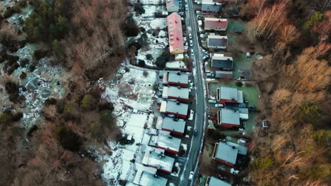 aerial forward view of nordic village developed along a road in the midst of trees and snow