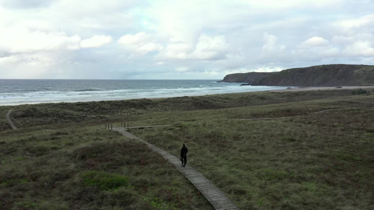 vista trasera del hombre caminando solo en el camino y las dunas que conducen a la playa desierta