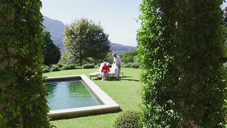 Glückliches-Kaukasisches-älteres-Paar,-Das-Auf-Einer-Sonnenliege-Im-Sonnigen-Garten-Sitzt-Und-Eine-Tasse-Kaffee-Trinkt