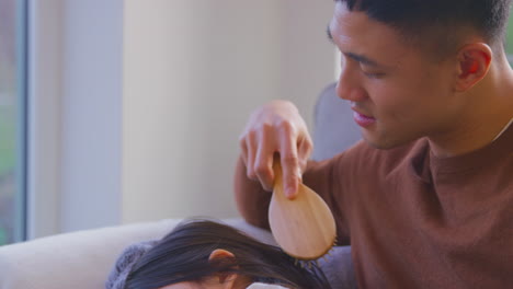 family having fun at home with dad brushing daughter's hair sitting on sofa with toy