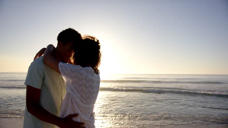 Una-Pareja-Birracial-Se-Abraza-Amorosamente-En-Una-Playa-Al-Atardecer-Con-Espacio-Para-Copiar