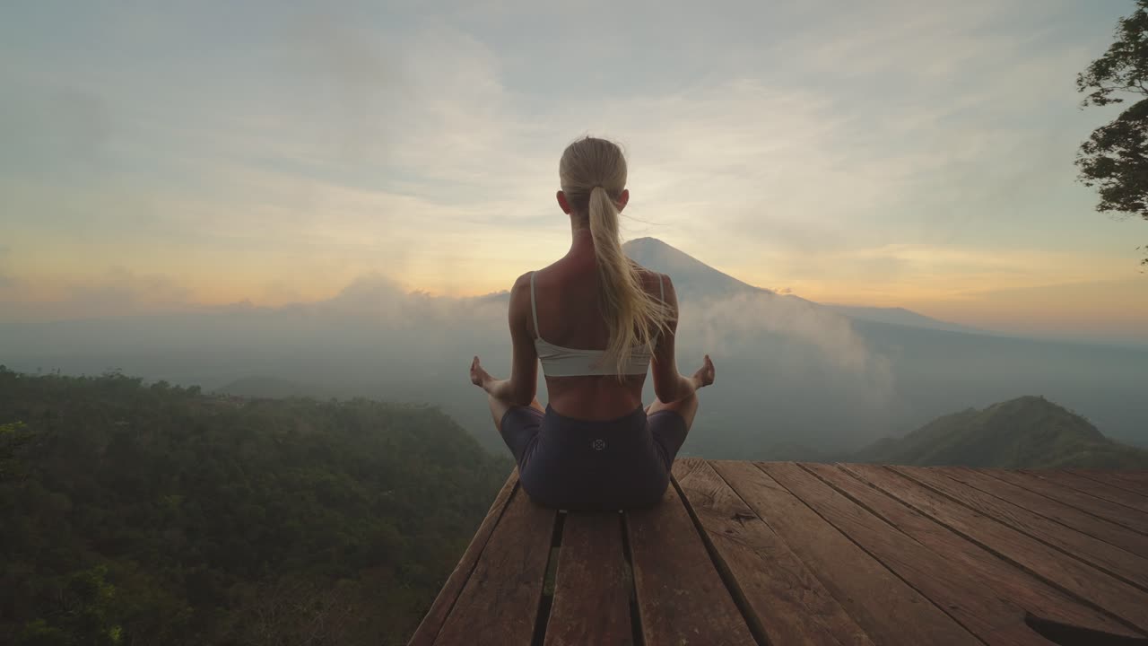 mujer en forma en ropa deportiva meditando en la plataforma con vista al monte agung, puesta de sol