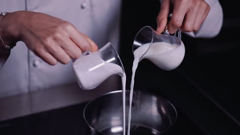 chef pouring two cups of fresh milk into a stainless pot - slow motion