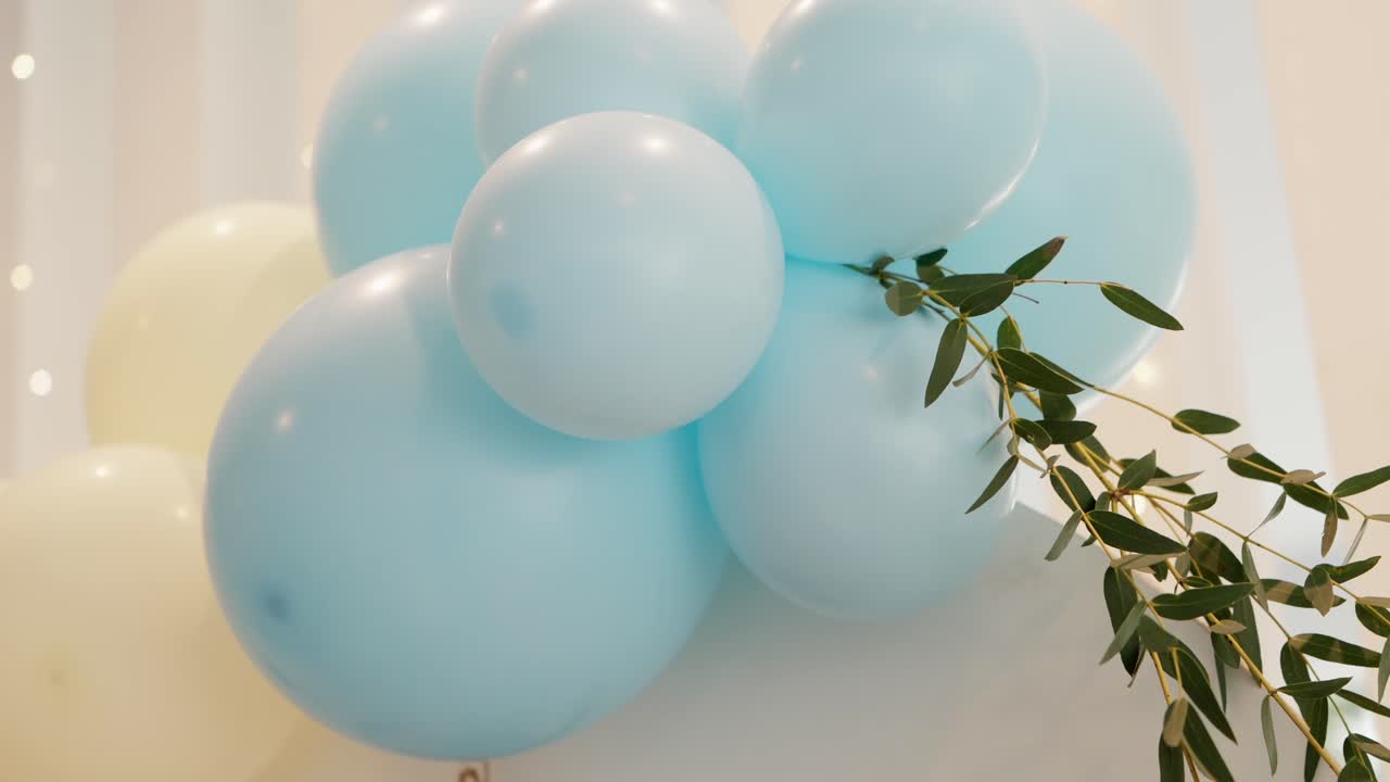 Cluster of pastel blue balloons with green leaves decoration hanging in a softly lit space