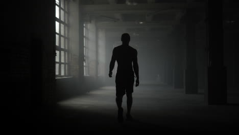 man silhouette walking in dark corridor. athlete taking break after workout