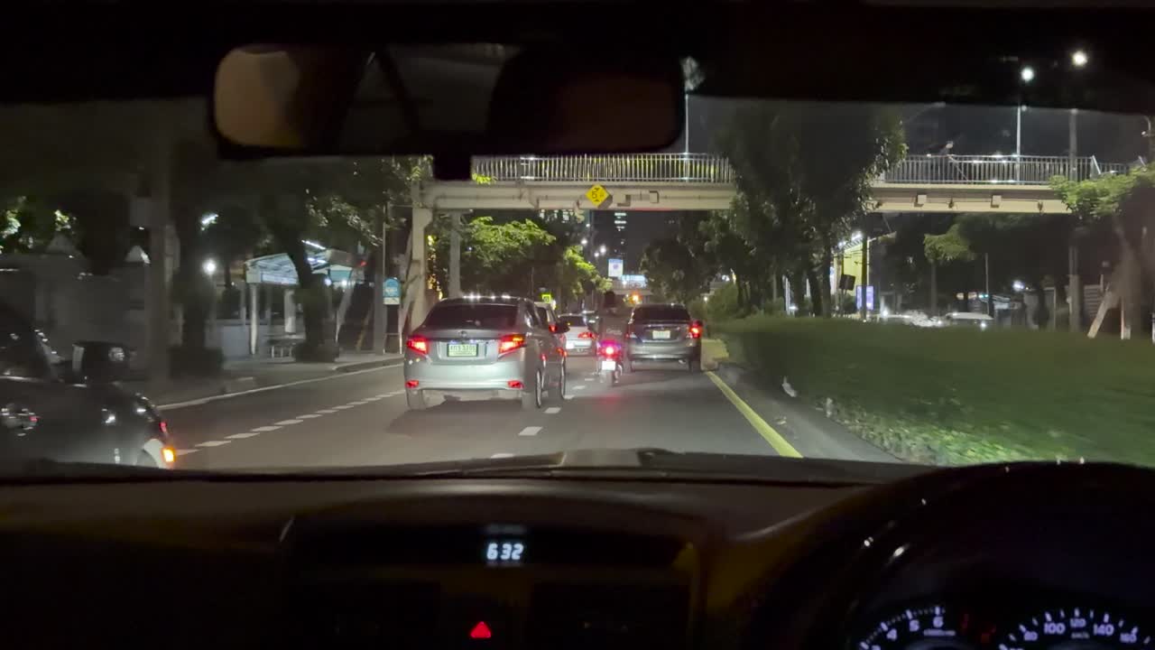 Dashboard view of taxi driving through city streets at night, illuminated by streetlights and headlights