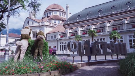 People-are-walking-along-the-spa-promenade-whilst-others-are-taking-pictures-and-selfies-in-the-city-center-of-Meran,-near-the-Kurhaus