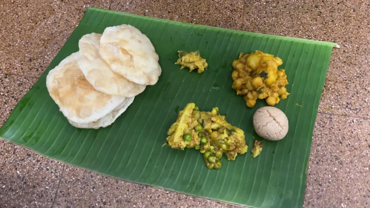 Bengali food platter with puri, dal, sabji and rosogolla served in a banana leaf.