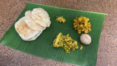 bengali food platter with puri, dal, sabji and rosogolla served in a banana leaf.
