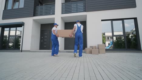 two young workers of removal company unload boxes and furniture from minibus into customer's home