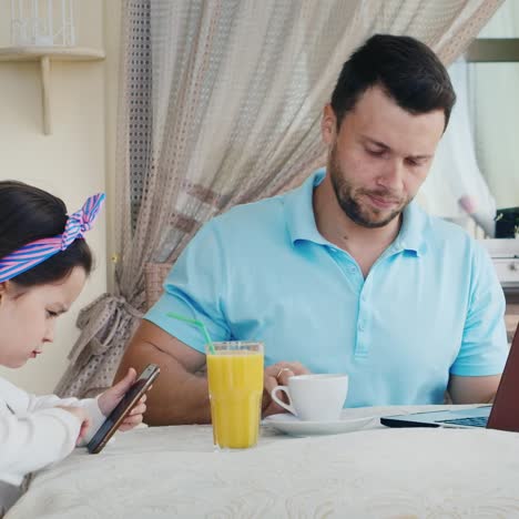 man uses laptop as daughter uses smartphone