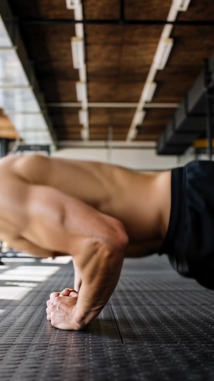 Vertical video: Starting low, shirtless man doing fist pushups on rubber floor for chest