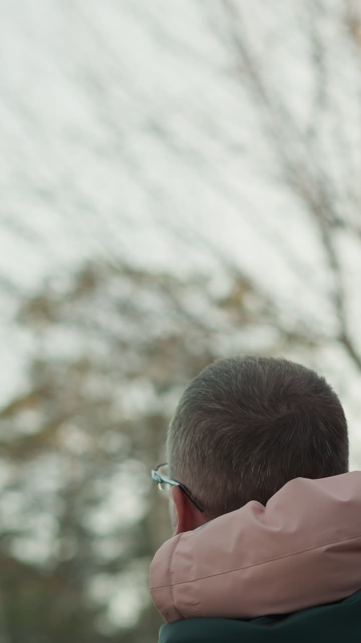 se ve a un hombre con una chaqueta verde cargando a su hija pequeña, que está vestida con una jaqueta rosa y una gorra a juego, mientras señala hacia el cielo