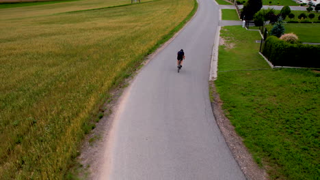 rear tracking aerial follows cyclist coasting down rural road in neighborhood