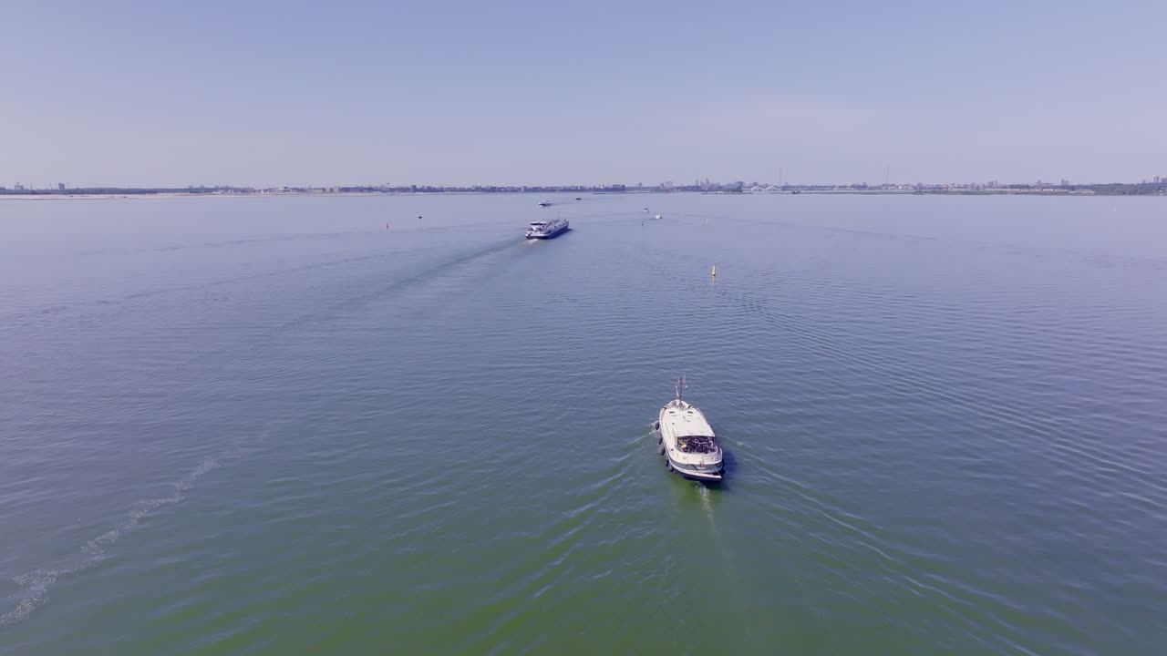 Aerial footage of a classic Luxemotor Dutch boat navigating calm waters in the province of Flevoland, The Netherlands, with another vessel visible in the background under a bright blue sky