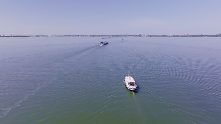 Aerial footage of a classic Luxemotor Dutch boat navigating calm waters in the province of Flevoland, The Netherlands, with another vessel visible in the background under a bright blue sky