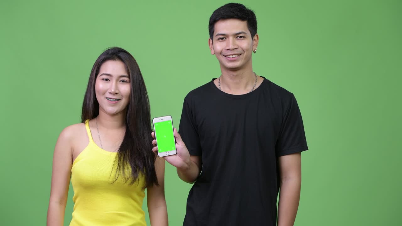 젊은 아시아 커플이 함께 전화를 보여주고 있습니다.
