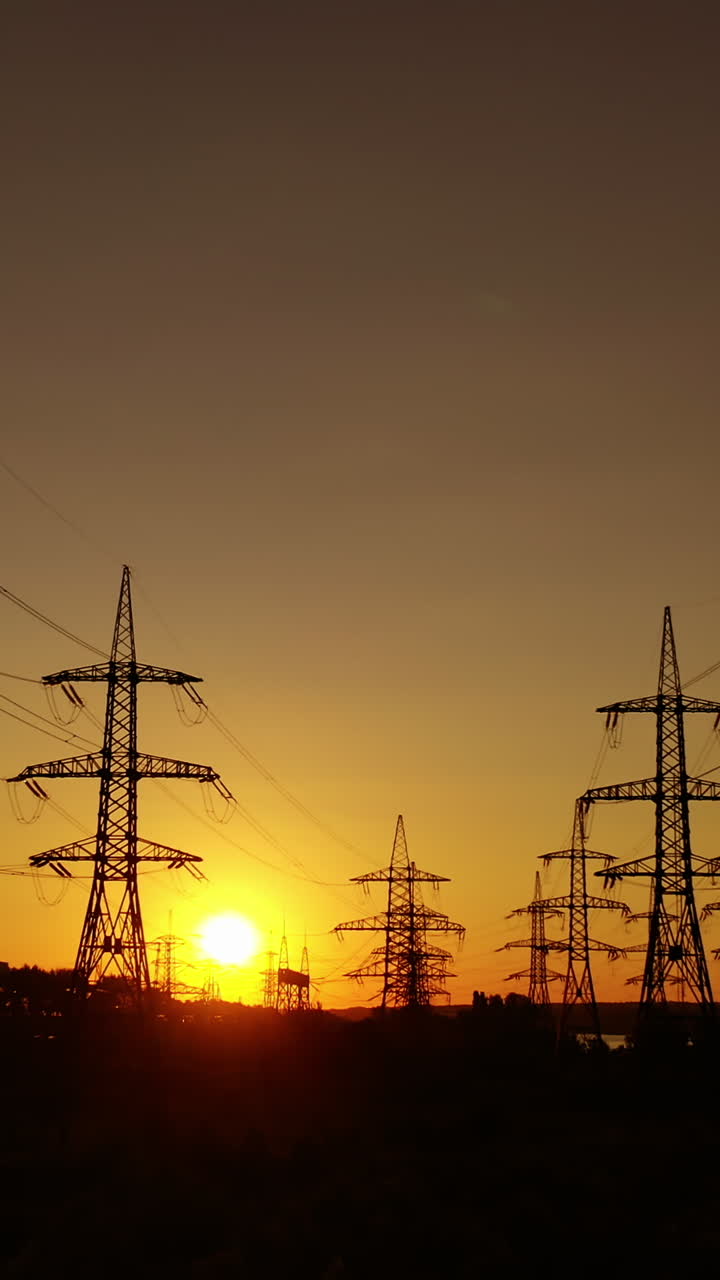 Transmission towers at dusk. Electric pylons near the smoking industrial pipe in the evening. Electric high voltage lines against beautiful orange sky at sunset. Energy efficiency conception. Vertical video