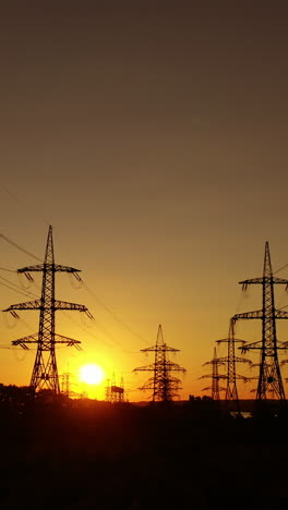 transmission towers at dusk. electric pylons near the smoking industrial pipe in the evening. electric high voltage lines against beautiful orange sky at sunset. energy efficiency conception. vertical video