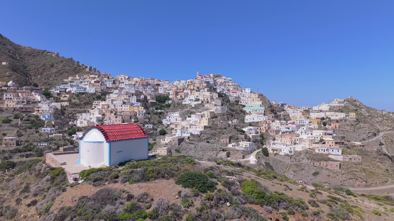 Cinematic drone pull back revealing a small chapel above the traditional village of Olympos, Karpathos Island. Stunning aerial view of Greek heritage and mountain landscape