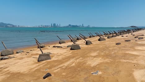 Vuelo-De-Drones-Sobre-La-Playa-Dorada-En-La-Isla-Kinmen,-金門,-Quemoy,-Con-Muchos-Picos-Anti-aterrizaje-Y-El-Horizonte-De-China-Al-Fondo:-Guerra-Entre-Taiwán-Y-China