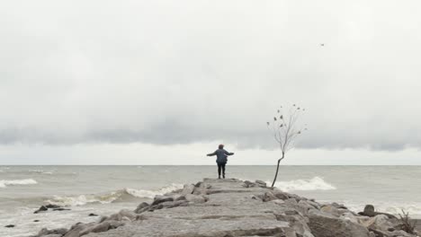 mujer solitaria parada pensativamente al final de un rompeolas de piedra en un día tormentoso