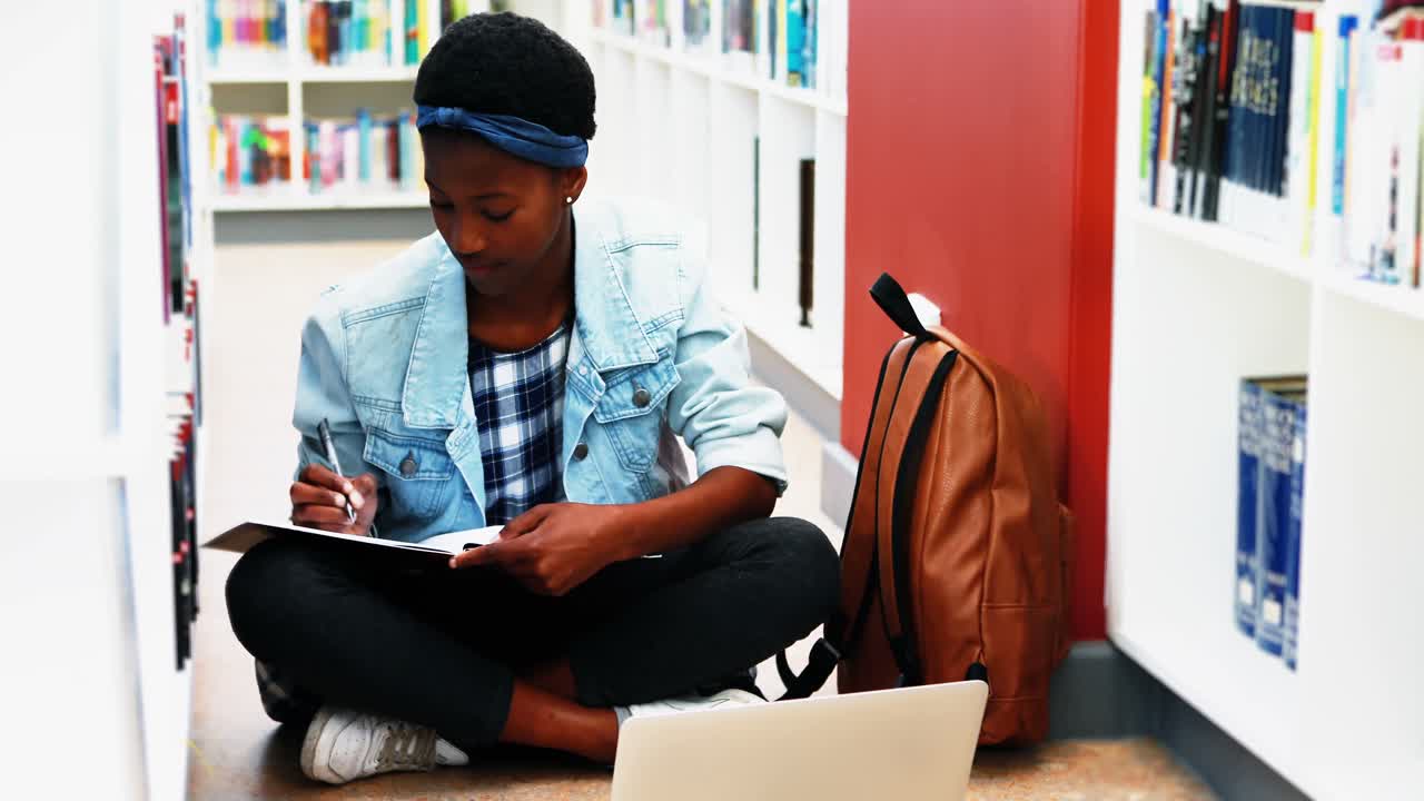 School girl doing home work while using laptop in library