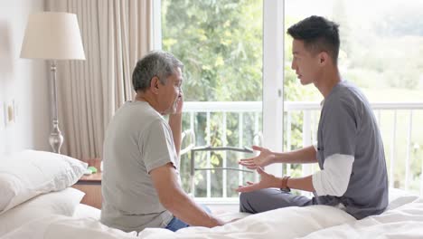 diverse male doctor discussing with senior male patient in bed at home, slow motion