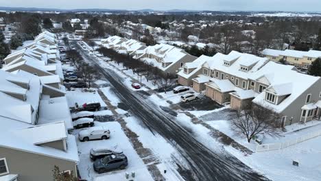 snowy neighborhood with uniform houses and parked cars along a cleared street