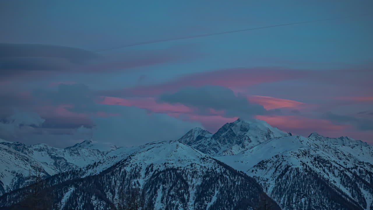 Nuvole che si muovono sopra le montagne innevate mentre un tramonto colorato sfuma nel crepuscolo - time-lapse