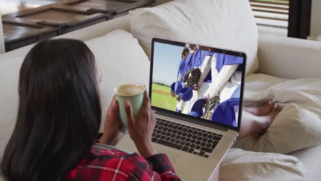 Compuesto-De-Mujer-Sentada-En-Casa-Sosteniendo-Un-Café-Viendo-Un-Partido-De-Béisbol-En-Una-Computadora-Portátil