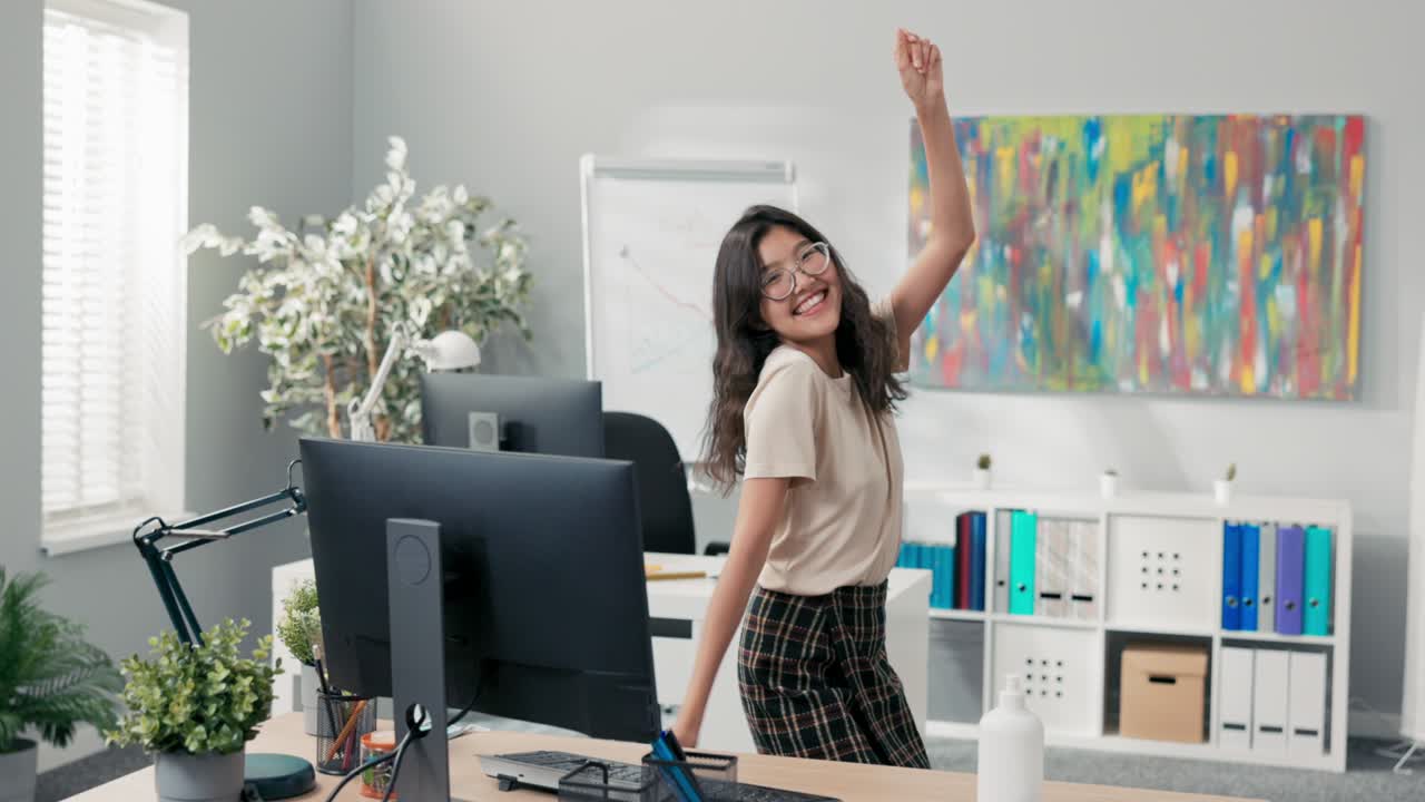 una mujer hermosa baila en una oficina, una empresa, una corporación entre los escritorios de los compañeros de trabajo, ella es feliz, sonriendo alegre, termina su trabajo temprano, obtiene un ascenso, cambia de posición