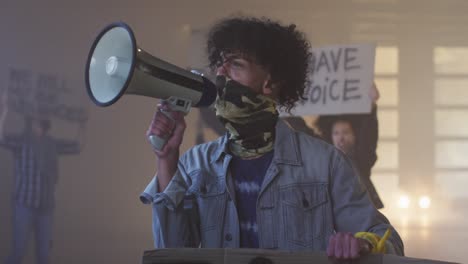 Diverse-group-of-people-wearing-face-masks-holding-protest-signs-shouting-into-megaphone