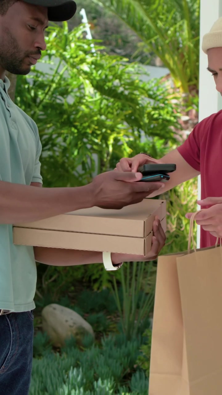 Vertical video: Checking phone, driver in blue polo tapping to confirm pizzas, handing to resident