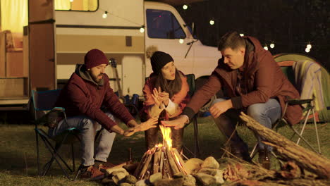 Close-friend-sitting-on-camping-chairs-around-camp-fire